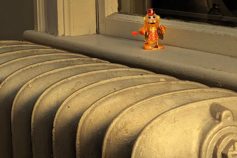 Painted cast iron radiator below a window sill in warm afternoon light, a small toy figure standing on the sill above it