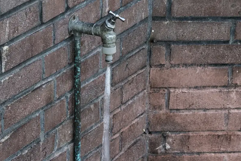 Outdoor spigot on a brick wall with a thick column of ice running from the spout down the pipe to the ground