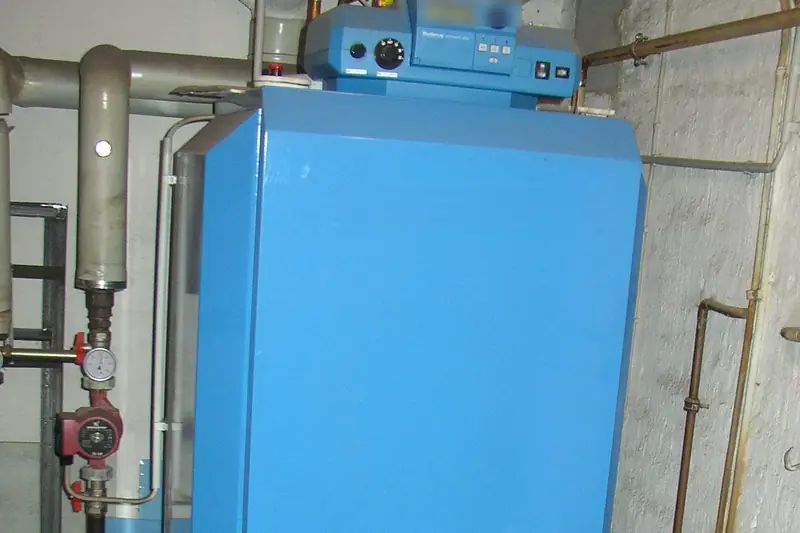 Blue oil-fired boiler standing in a whitewashed stone basement, its control panel on top and copper and steel heating pipes running along the walls